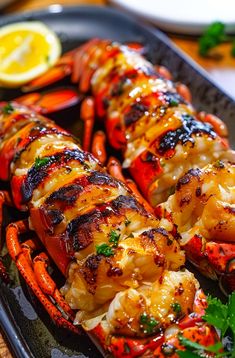 grilled lobsters on a black platter with lemon wedges and parsley