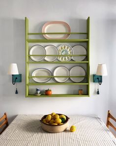 a bowl of fruit on a table with plates and bowls hanging from the wall behind it