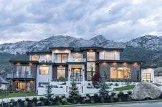 a large house with mountains in the background at dusk, surrounded by greenery and landscaping