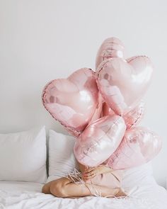 a woman laying on top of a bed covered in pink heart shaped balloons