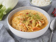 a white bowl filled with soup next to two spoons and some celery