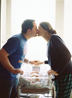 a man and woman kissing while standing next to a baby in a crib