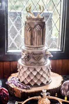 a three tiered cake sitting on top of a wooden table next to a window