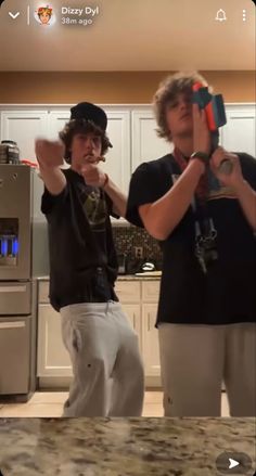 two young men standing in a kitchen holding up their hands to take a selfie