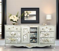 a white dresser with flowers painted on the doors and drawers is in front of a painting