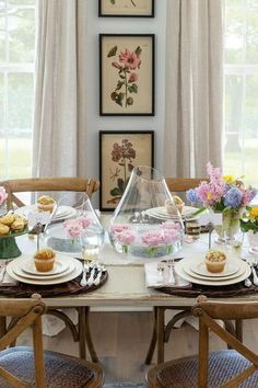 a dining room table set for two with flowers in vases and cupcakes on plates