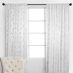 a white chair sitting in front of a window next to a curtain with an ornate pattern