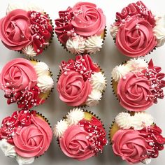 twelve cupcakes with pink and white frosting roses on top, decorated with sprinkles