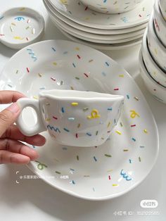 a hand holding a coffee cup with sprinkles on it next to plates