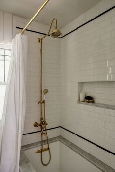 a bathroom with white tile and black trim on the walls, along with a gold shower head