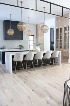 a large kitchen with wooden floors and white counter tops, along with modern pendant lights hanging from the ceiling