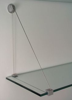 a glass shelf with a metal hook hanging from it's side on the wall