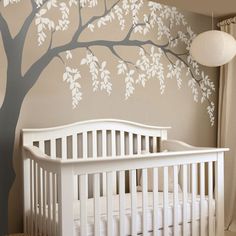 a baby's room with a tree painted on the wall and crib next to it