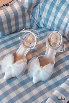 a pair of white high heeled shoes sitting on top of a blue and white checkered bed