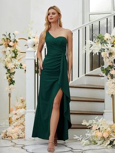 a woman wearing a green dress standing in front of some flowers and stairs with her legs crossed