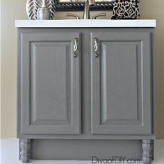 a bathroom vanity with gray cabinets and white countertop, decorated with black and gold accessories