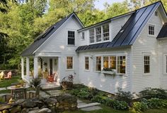 a white house with a black metal roof and windows on the front porch is surrounded by greenery