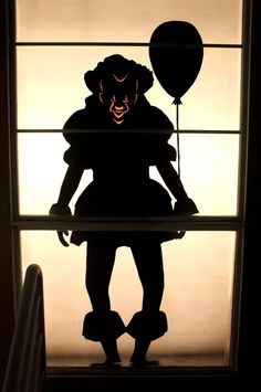 a silhouette of a person holding a balloon in front of a window with the shadow of a clown on it