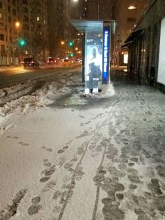 a bus stop sitting on the side of a road covered in snow next to tall buildings