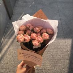 a person holding a bouquet of pink roses on the sidewalk in front of a building