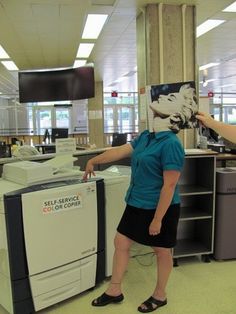 two women standing in an office area with computers and printer equipment on the desks