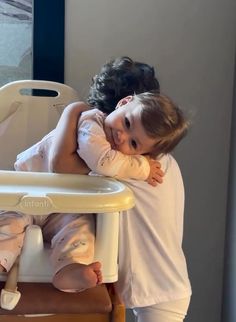 a woman holding a small child in her arms while sitting in a highchair