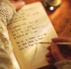 a hand holding a pen and writing on an open book