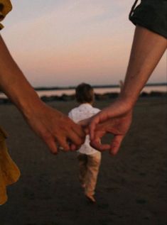 two people holding hands while walking on the beach at sunset or dawn with one person reaching out to touch the other's hand