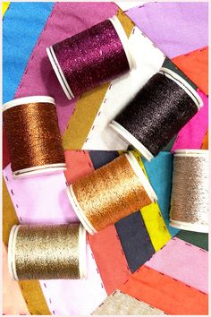 several spools of thread sitting on top of a colorful quilting material background