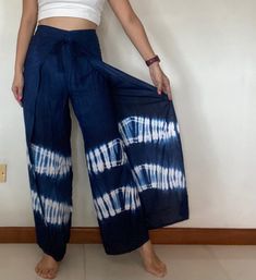 a woman standing in front of a white wall holding onto a blue tie - dyed pants