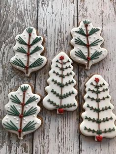 four decorated cookies with white icing and christmas trees on them sitting on a wooden table