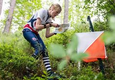 a woman in the woods looking at a map while holding a camera and reading it