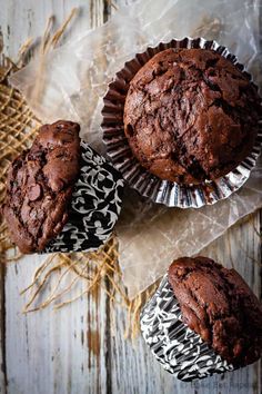 three chocolate muffins sitting on top of paper wrappers next to each other