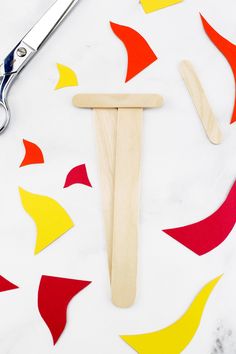 a pair of scissors next to some cut out shapes on a white table with red, yellow and orange paper