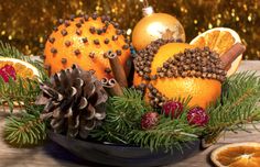 an arrangement of oranges and pine cones in a bowl on a table with christmas decorations