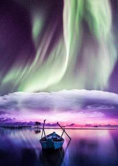 a boat floating on top of a lake under a purple and green aurora borel