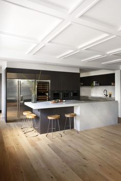 an open kitchen with wooden floors and white counter tops, along with bar stools