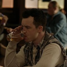 a man sitting at a table drinking from a glass in front of another man with his hand on his head