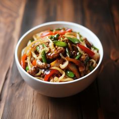 a white bowl filled with noodles and vegetables on top of a wooden table next to a fork