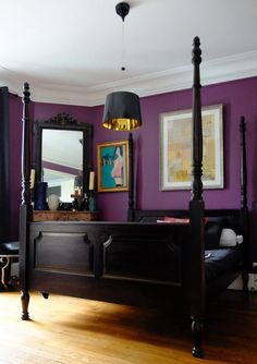 a bedroom with purple walls and wooden floors is pictured in this image, the bed has four posts