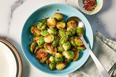 a blue bowl filled with brussel sprouts next to a white plate