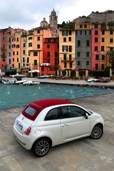 a small white car parked in front of a body of water next to colorful buildings