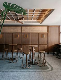 an empty bar with stools and tables in the corner, next to a tall palm tree