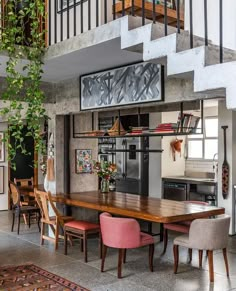 a dining room table with pink chairs and an open staircase leading up to the second floor