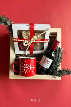 a red coffee mug sitting on top of a wooden box filled with food and wine