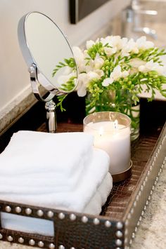 a tray with candles, flowers and towels on it next to a sink in a bathroom