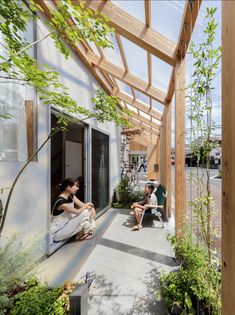 two people sitting on a porch next to trees and plants in front of a building