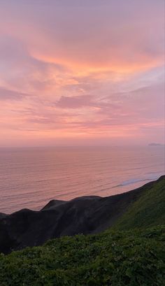 a bench sitting on top of a lush green hillside next to the ocean at sunset