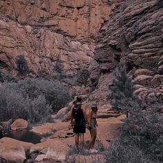 two people standing in front of some rocks and water at the base of a mountain