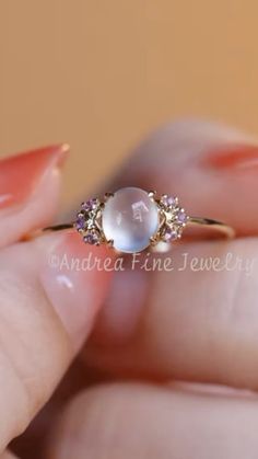 a woman's hand holding an engagement ring with a white pearl and pink stones